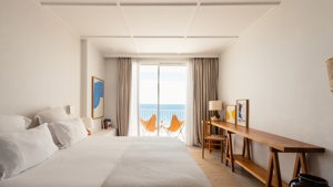 A well-organized bedroom features a cozy bed, a chair by the table, and a balcony with a wonderful ocean view.