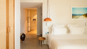 A well-organized bedroom features a cozy bed, a hanging lamp on the left, and a portrait mounted above the bed.