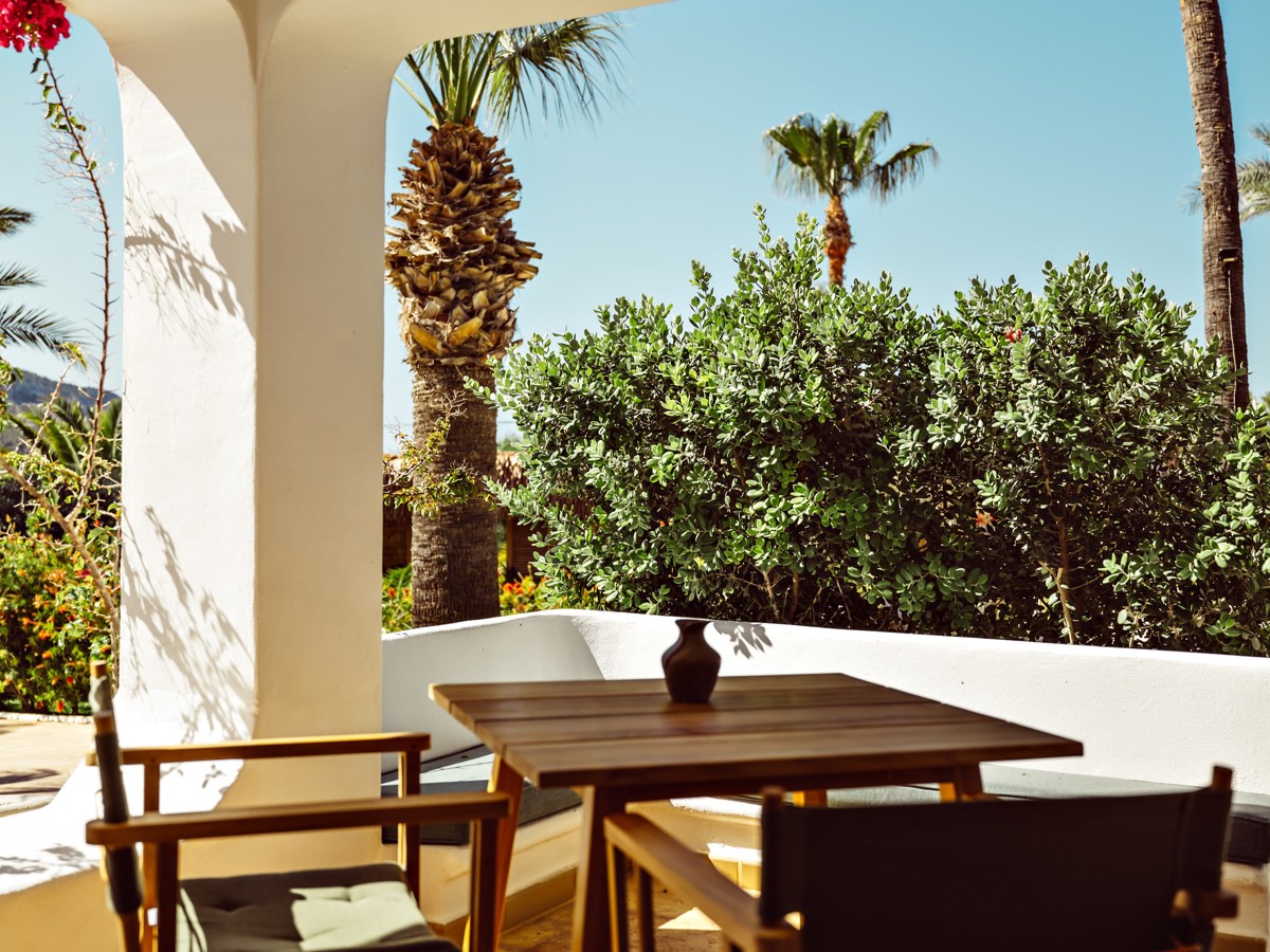 Une table avec deux chaises est placée à l'extérieur, offrant une vue magnifique sur les plantes et les arbres.