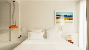 A well-organized bedroom features a cozy bed, a side table with a lamp, and portraits above.