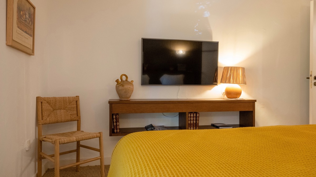 Un téléviseur est fixé au mur au-dessus du meuble, juste en face du lit douillet.