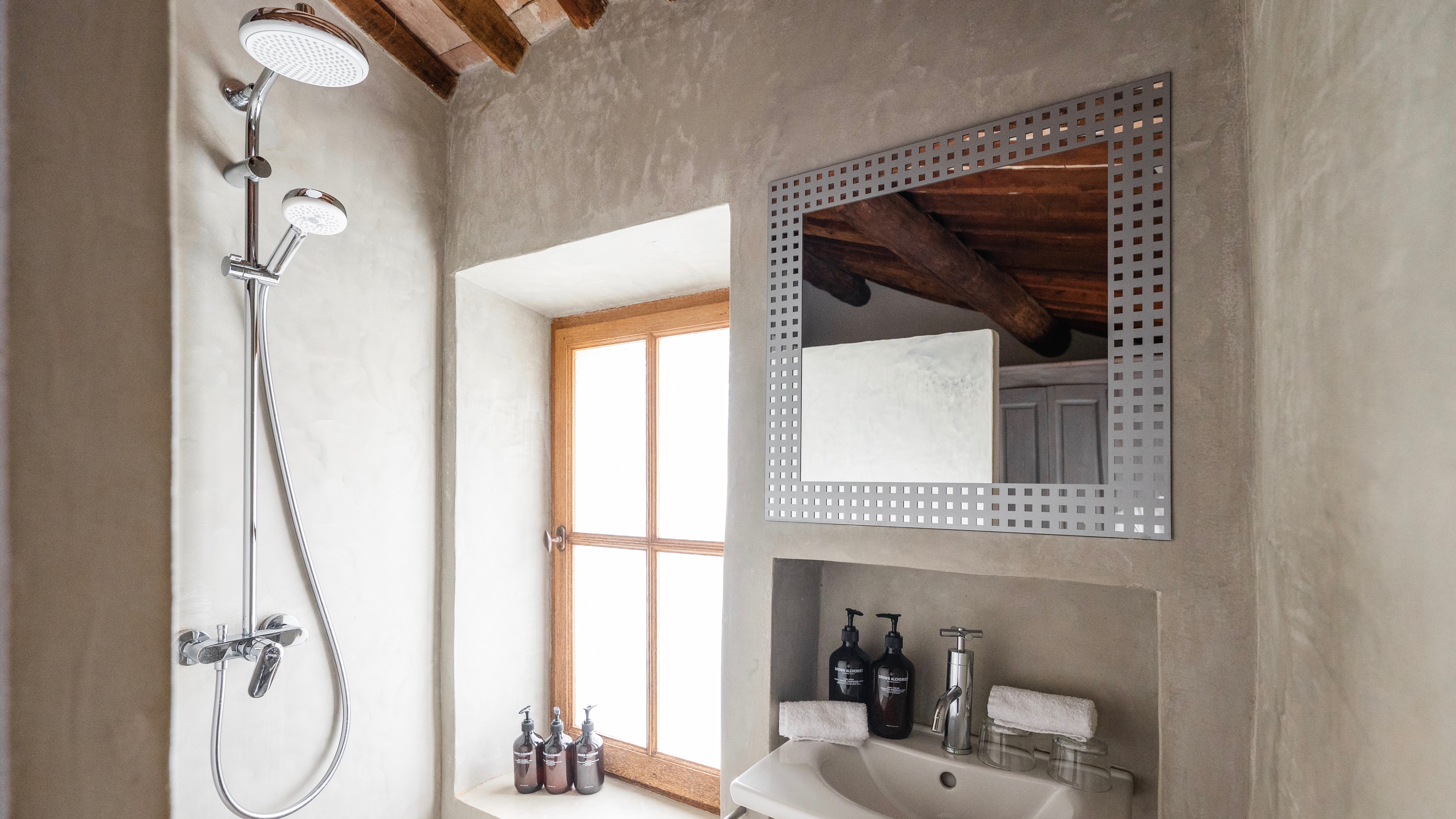 Rustic bathroom in the Le Galinier room, featuring a shower, sink, mirror, and a bright window