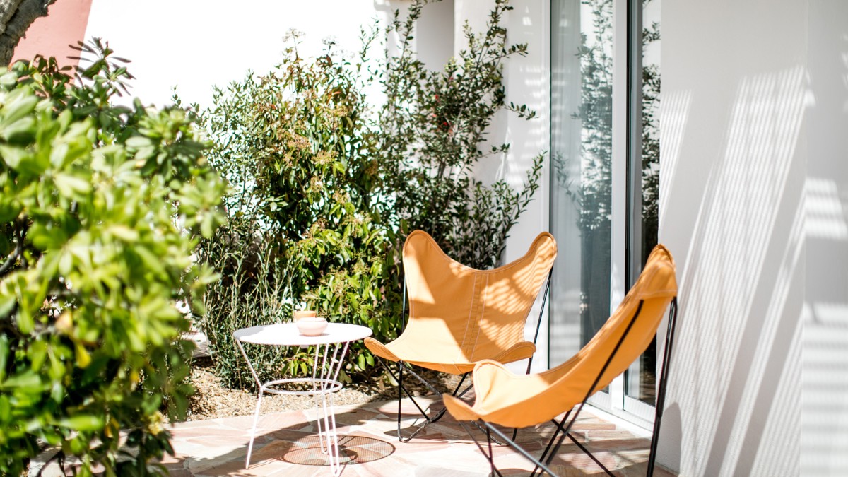 Two relaxing chairs with a table are placed in the lawn area near the glass door.