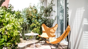 Two relaxing chairs with a table are placed in the lawn area near the glass door.