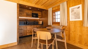 A clicked photo of the kitchen area features a round dining table with four chairs nearby.