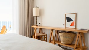 A chair is placed near a table holding a lamp, a portrait, and a notebook.