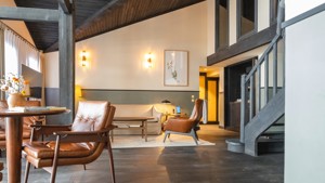 Un espace de vie comprend un canapé confortable installé près des escaliers, avec des portraits montés au-dessus.