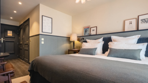 Une chambre comprend un lit confortable, une table de chevet avec une lampe et des portraits au-dessus.