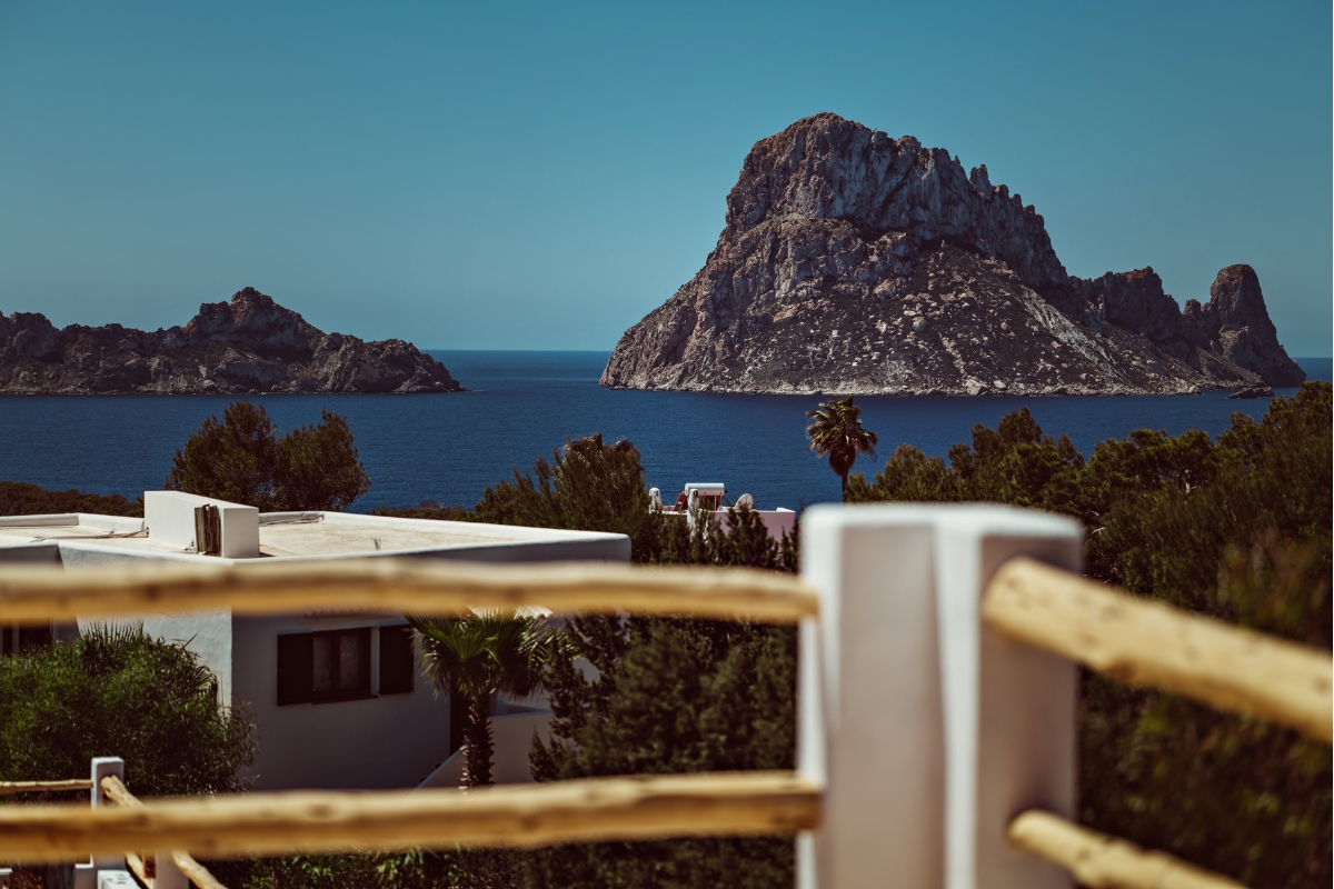 Scenic view of rocky island, deep blue sea, white villas, and lush green trees under clear sky.