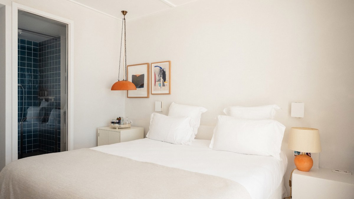 A well-organized bedroom features a cozy bed with side tables holding lamps and two portraits above.