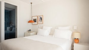 A well-organized bedroom features a cozy bed with side tables holding lamps and two portraits above.