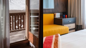 An orange-colored cozy sofa is placed right beside the balcony door.