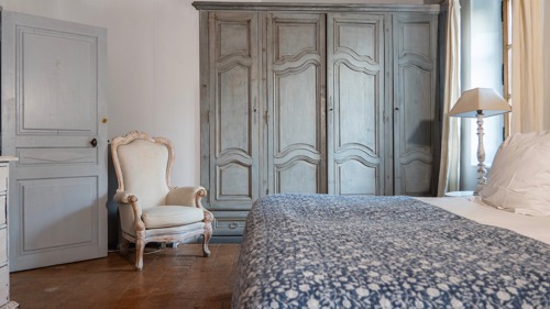 Chambre rangée avec lit confortable, lampe d'appoint et chaise près d'étagères grises.