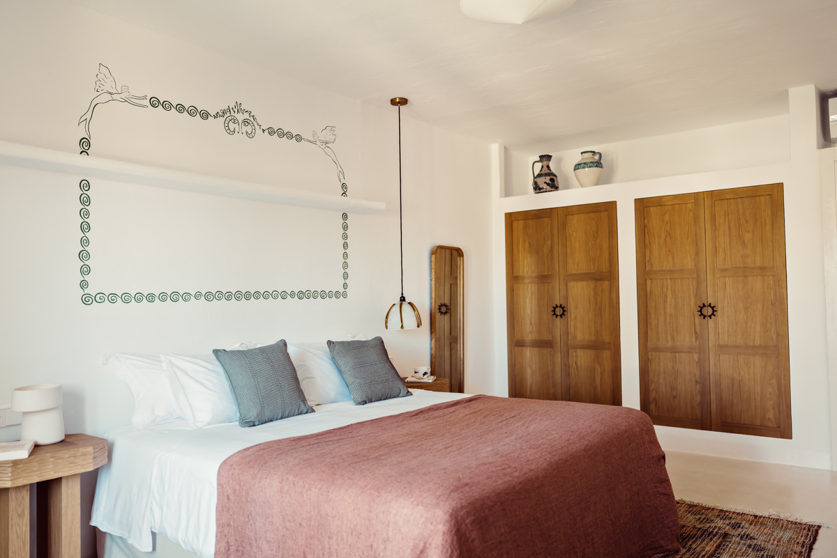 Chambre confortable avec lit double, coussins gris, armoire en bois, station café et fresque murale.