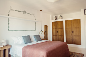 Chambre confortable avec lit double, coussins gris, armoire en bois, station café et fresque murale.