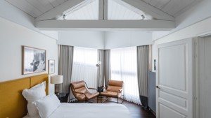 A bedroom features two cozy chairs beside the bed and two portraits mounted above.