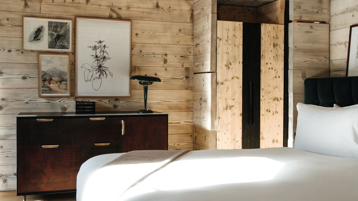 Different-sized portraits adorn a wooden-finished wall above a table with a unique lamp.