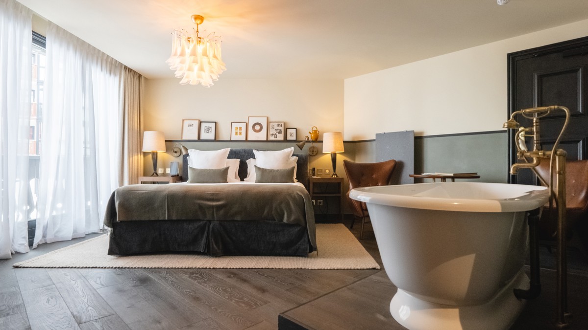 Une chambre luxueuse comprend un lit douillet, une baignoire à droite et des portraits au-dessus.