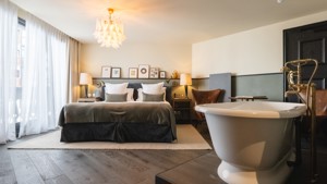 Une chambre luxueuse comprend un lit douillet, une baignoire à droite et des portraits au-dessus.