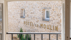 Le nom "HOTEL LE MOULIN" imprimé sur le mur à texture rugueuse est visible depuis le balcon.