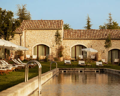 A sunny outdoor pool and patio area outside stone guest rooms at Capelongue in Provence.