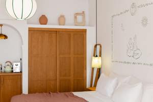 Chambre chaleureuse avec meubles en bois, fresque murale de deux figures, lumière douce et vases décoratifs.