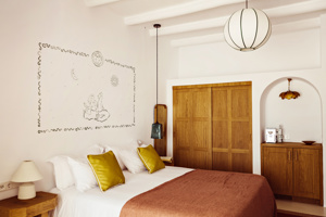 Chambre confortable avec placards en bois, décoration murale artistique, couverture rose et lumière naturelle venant de la fenêtre.