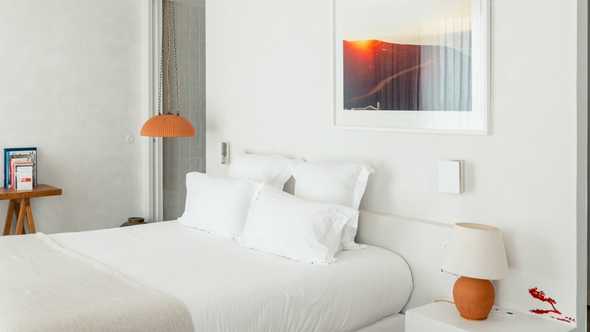 A well-organized bedroom features a cozy bed, a side table with a lamp, and a portrait mounted above the bed.