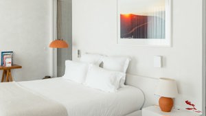 A well-organized bedroom features a cozy bed, a side table with a lamp, and a portrait mounted above the bed.