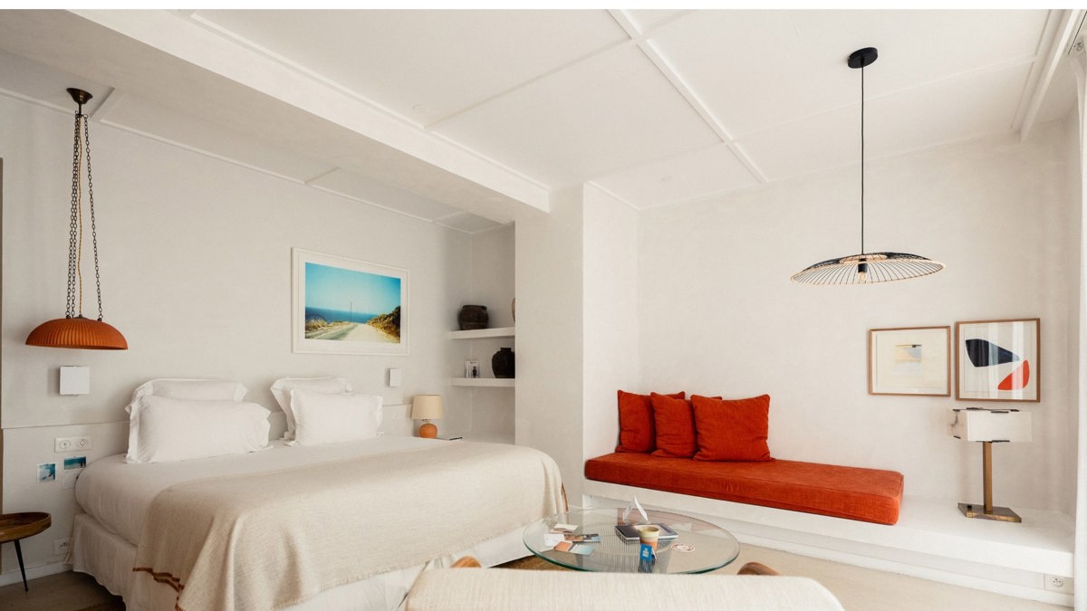 A well-organized bedroom features a cozy bed, a side table holding a lamp, and portraits mounted overhead.