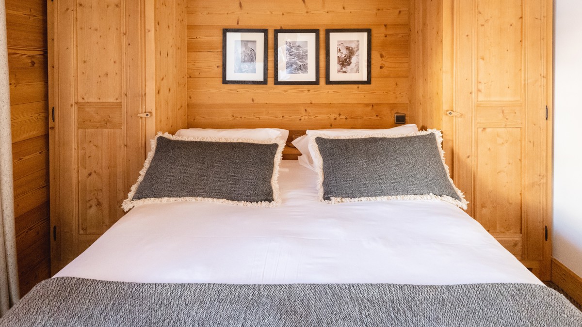 A bedroom features a cozy bed with three portraits mounted on the wooden-finished wall above.