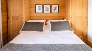A bedroom features a cozy bed with three portraits mounted on the wooden-finished wall above.