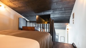 Un téléviseur sur pied est placé près de la rampe d'escalier, face au lit.