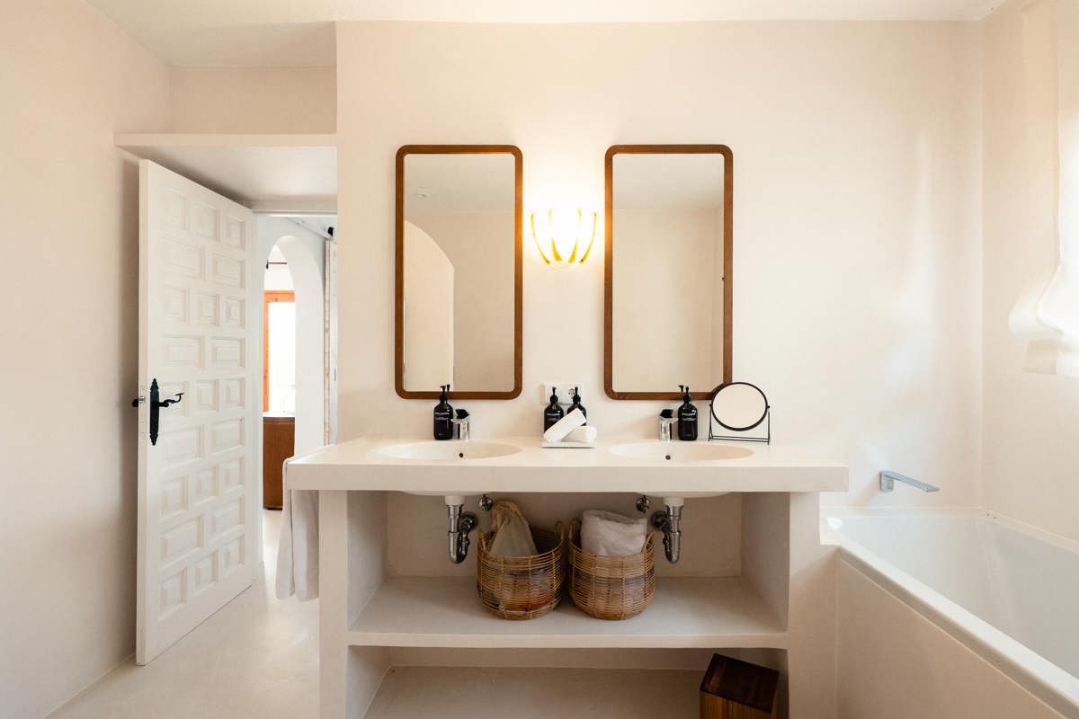 Salle de bain lumineuse avec double vasque, miroirs en bois, paniers en osier et baignoire blanche.