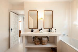 Salle de bain lumineuse avec double vasque, miroirs en bois, paniers en osier et baignoire blanche.