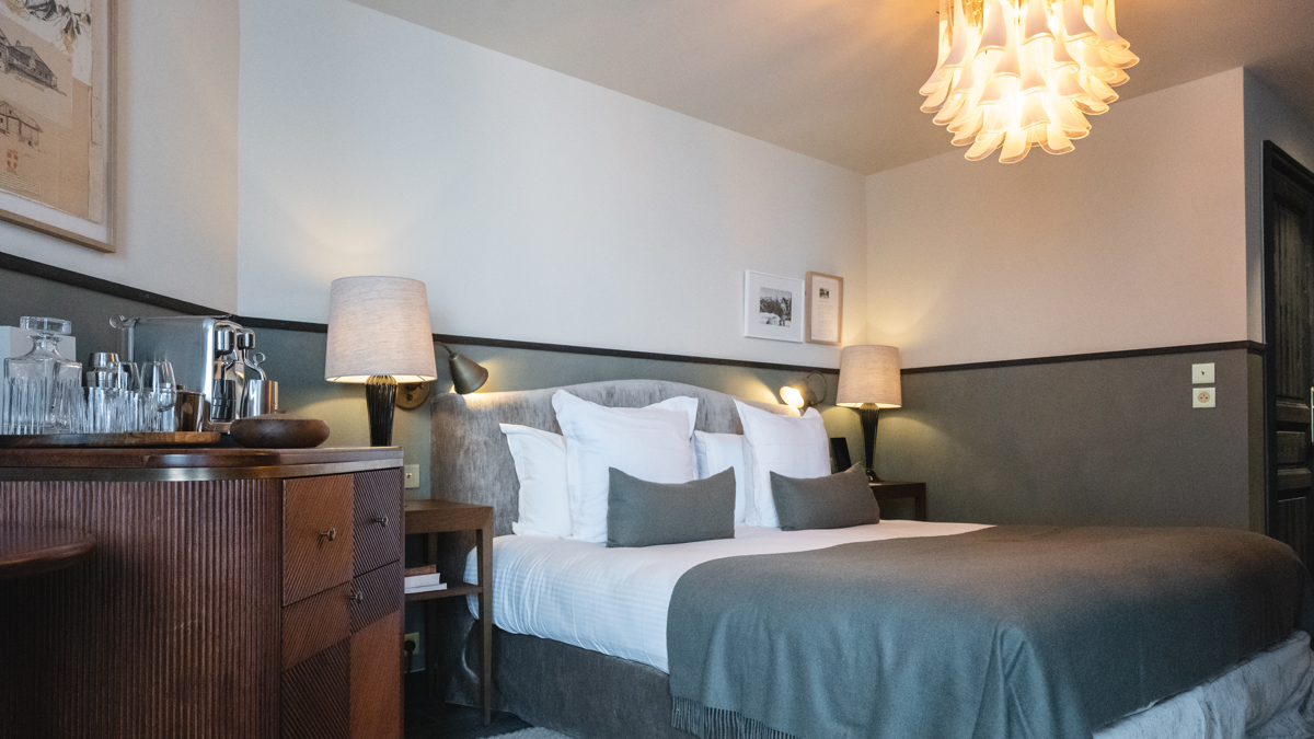 Chambre organisée avec lit confortable, table de chevet, lampe et lustre élégant suspendu.