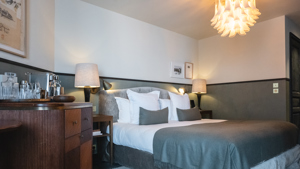 Chambre organisée avec lit confortable, table de chevet, lampe et lustre élégant suspendu.