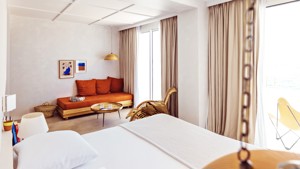 A well-organized bedroom features a cozy bed, a sofa chair in the corner, and portraits mounted above.