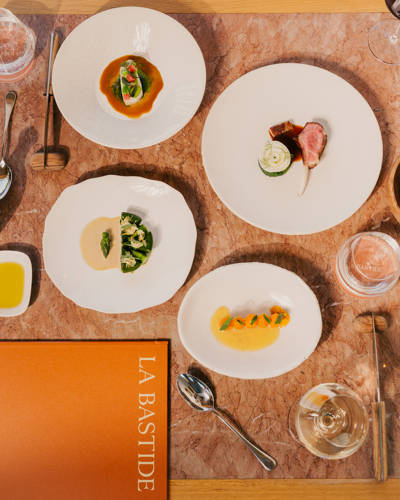 Top-down view of fine dining dishes and a menu laid out on a stone tabletop at La Bastide in Bonnieux.