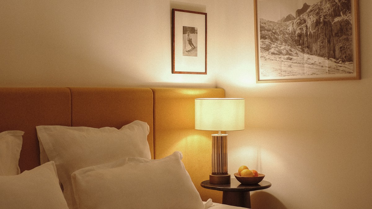 Two portraits are mounted above the bed’s side table, which holds a glowing lamp.