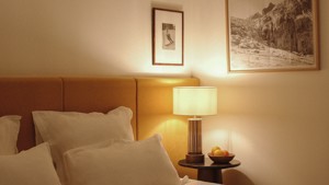 Two portraits are mounted above the bed’s side table, which holds a glowing lamp.