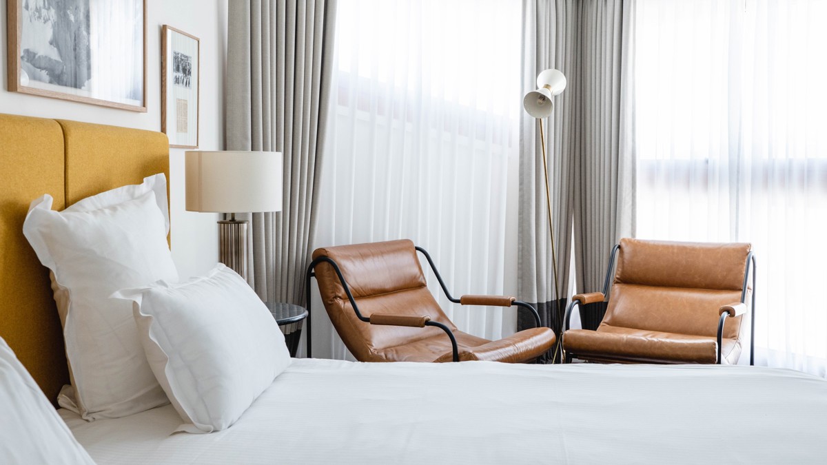 Two cozy chairs are placed beside the bed, near the curtain-covered glass window.
