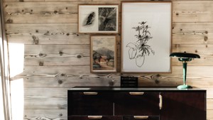 Different-sized portraits are mounted on the wooden-finished wall above a table with a unique lamp.