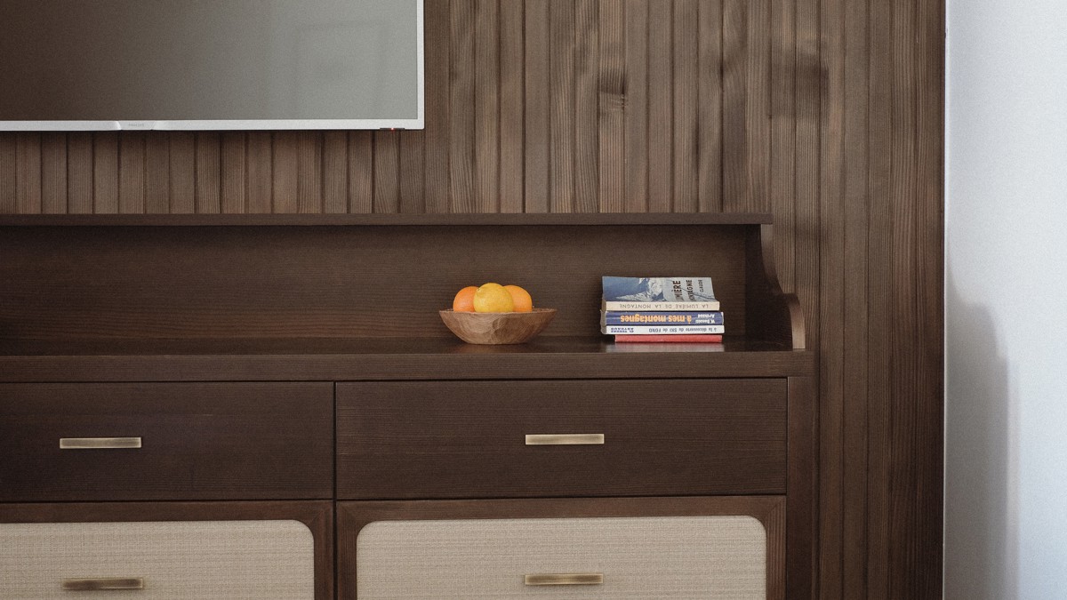 A fruit bowl and some notebooks are placed on the table below the mounted TV.