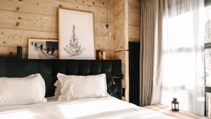 A cozy bed is placed near a large glass window with two portraits above.