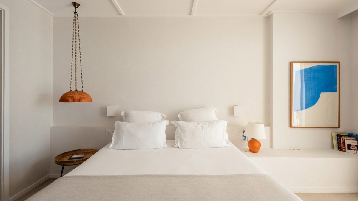 A portrait is mounted above a chair in the bedroom, with crockery and notebooks on the right wall shelves.