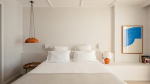 A portrait is mounted above a chair in the bedroom, with crockery and notebooks on the right wall shelves.