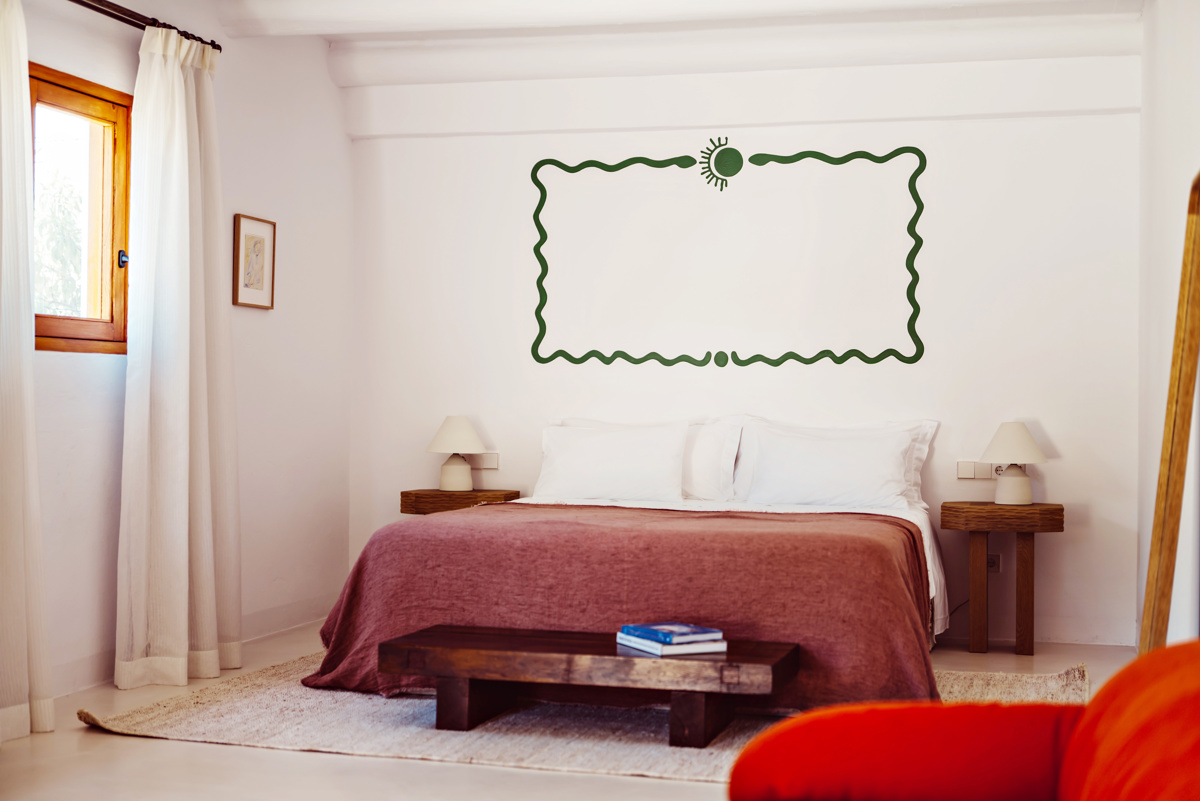 Chambre lumineuse aux murs blancs, décoration murale verte, meubles en bois et lit douillet à couverture rouge.