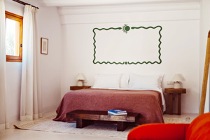 Chambre lumineuse aux murs blancs, décoration murale verte, meubles en bois et lit douillet à couverture rouge.