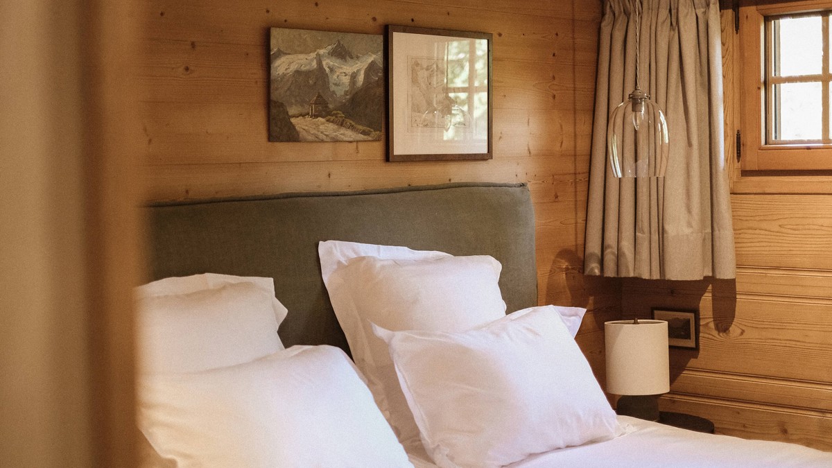 A cozy bed is placed by the wooden-finished wall with two portraits mounted above.
